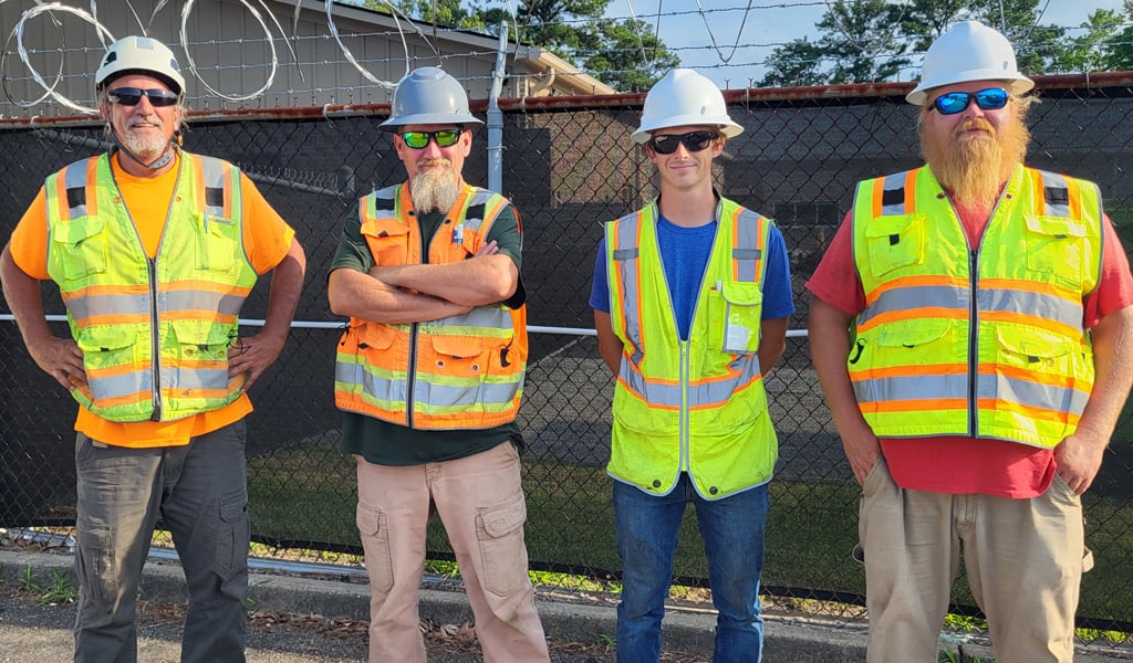 Four men stand together in safety vests preparing to perform rail survey.