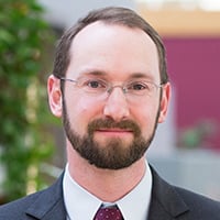 A person in a suit and tie is standing with an office background.