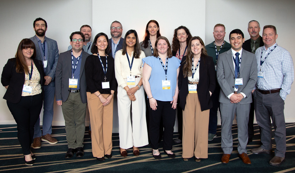 A group of 13 people all wearing business attire with conference badges around their necks. 