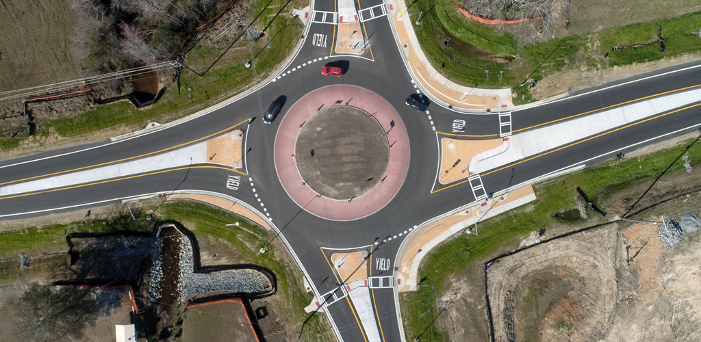 A roundabout road with two black cars and a red car.