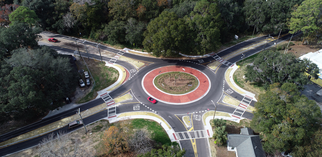A roundabout surrounded by trees with a red car driving around it.