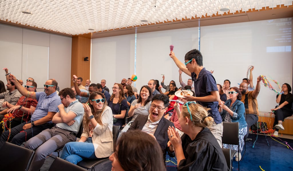 Employees celebrate Milestones with sunglasses, beach balls, and noisemakers in a conference room.