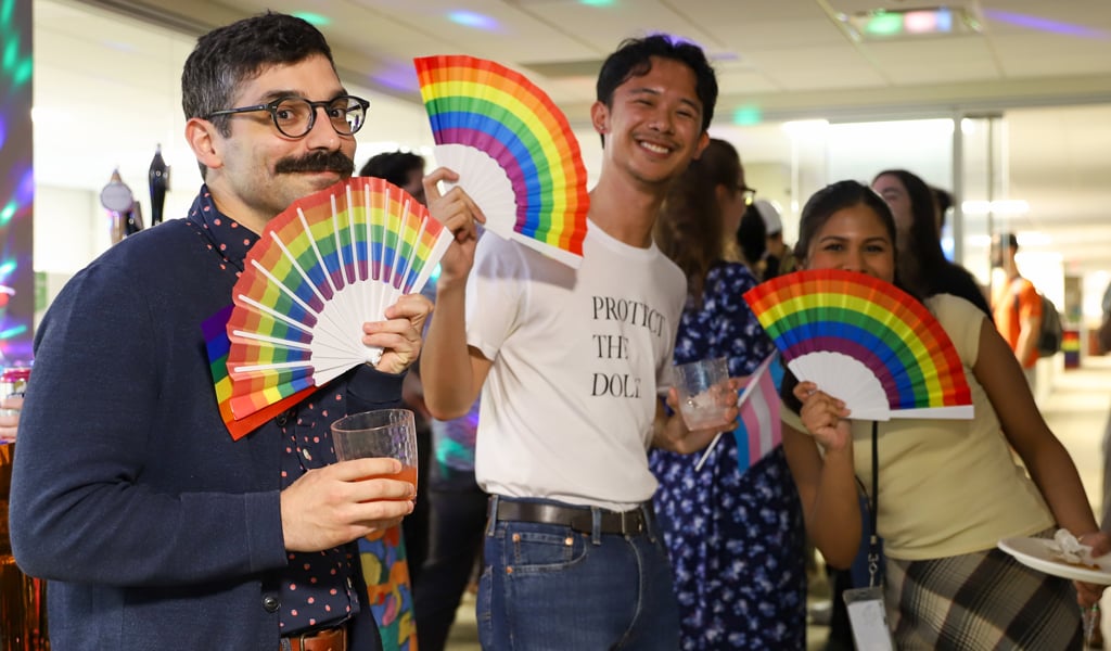 Employees hold rainbow paper fans while celebrating Pride event.