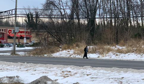 A pedestrian walks alongside a multi-lane roadway with no pedestrian facilities. 