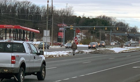 A pedestrian crossing a multi-lane roadway with no pedestrian crosswalk.  