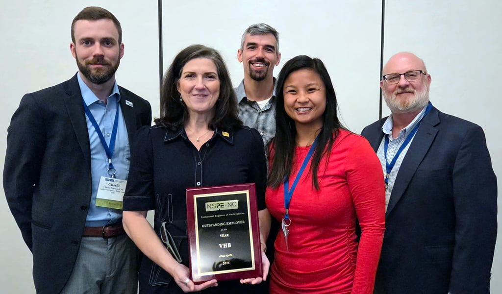 Five people stand side by side and pose for group photo, person in center holds award.