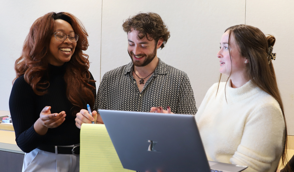 Three young people smiling and laughing while looking at a laptop.