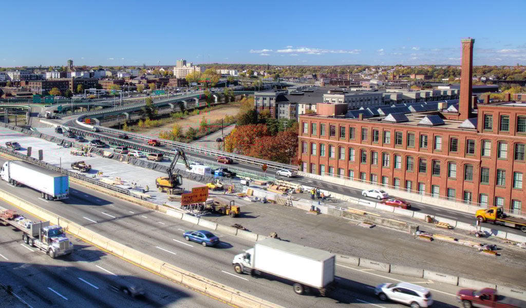 A major bridge cutting through the city of Providence under construction, with cars passing over the bridge.