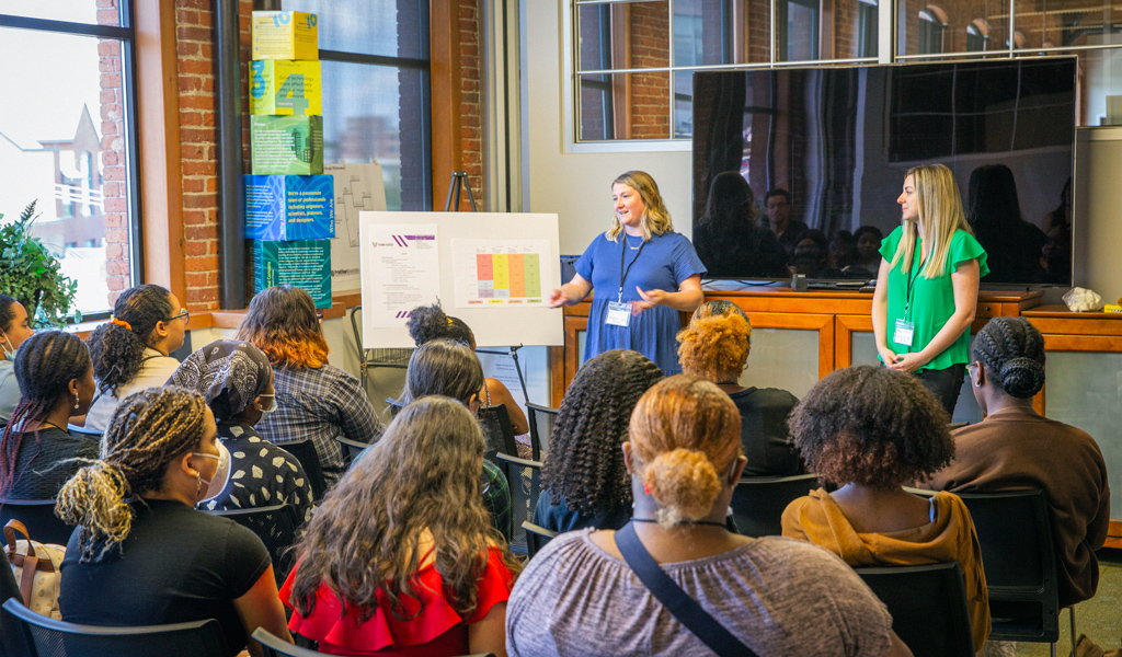 Two women teach a group of students in an office.