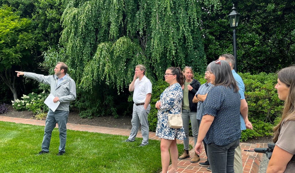 Phillip pointing to landscape features on the green grass next to attendees. 