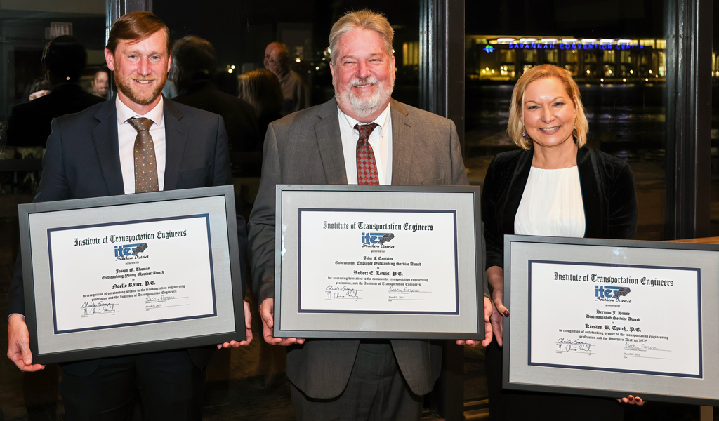 Three award winners stand together smiling at the camera holding their award plaque. 