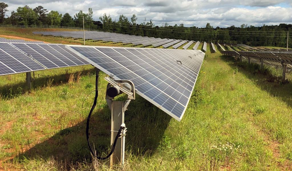 A large field with long rows of solar panels underneath a partly cloudy sky.