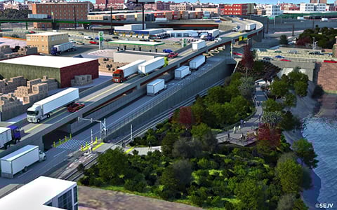 An aerial view of a bustling urban freight yard featuring trucks, trains, and various storage buildings adjacent to a water body, with a small, lush park area nearby.