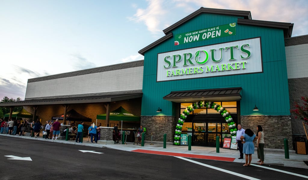 New green building with a large Sprouts sign and a balloon arch surrounding the entryway.