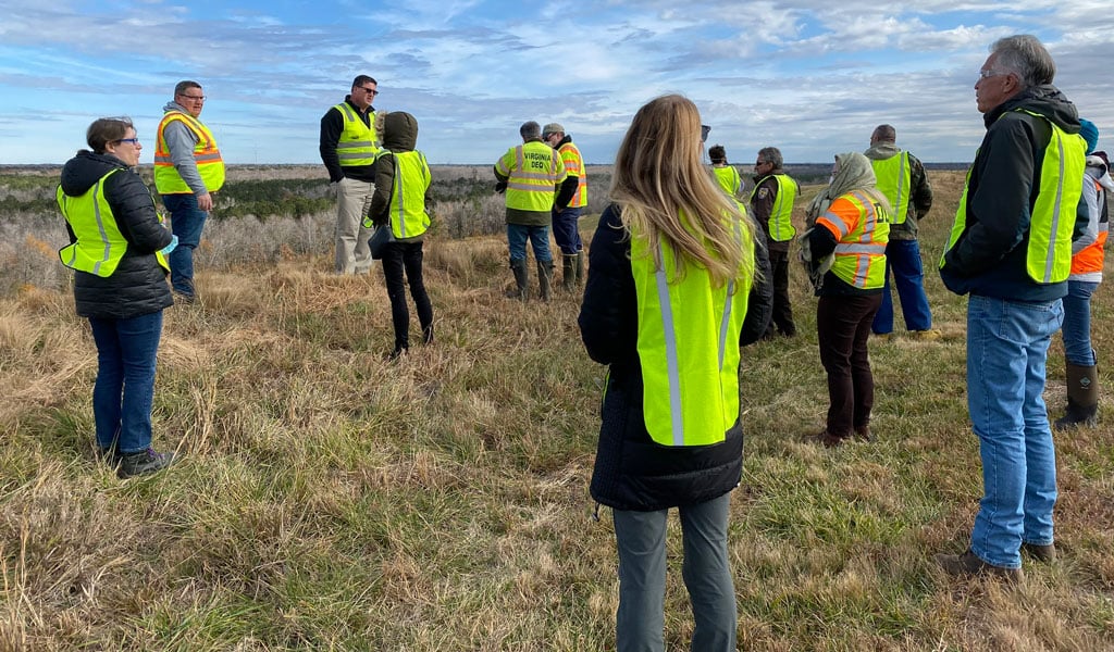 Group of tour participants in safety vests standing on a grassy capped landfill cell overlooking the surrounding landscape.