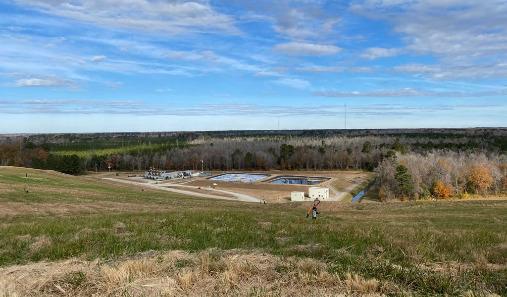 View from a closed landfill cell showing the landfill gas and stormwater management facilities below, surrounded by restored grassy slopes and forest.