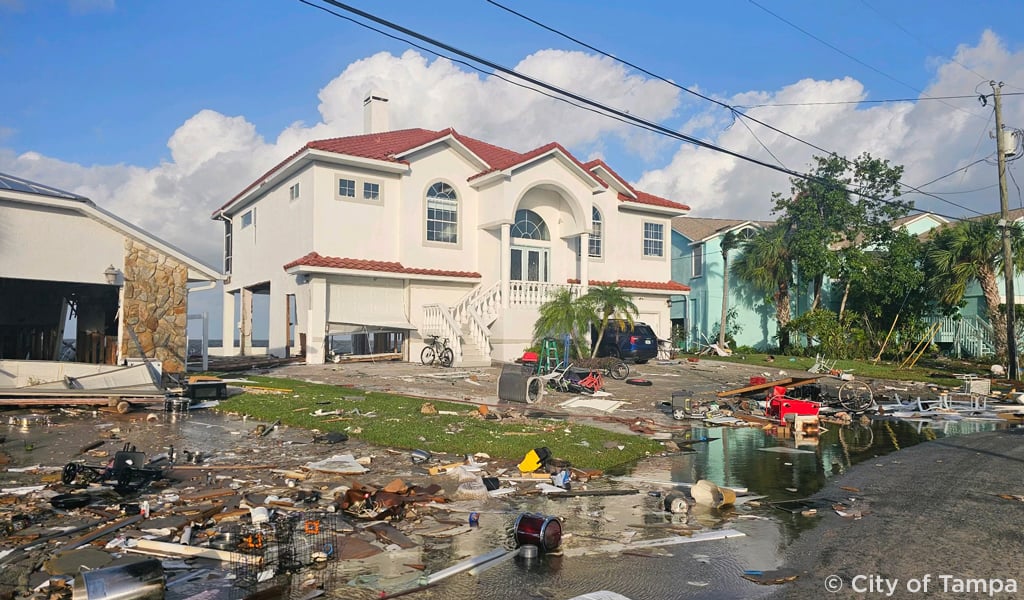 A two story house with hurricane debris on the lawn.