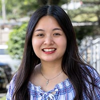 A person with long hair, wearing a blue and white checkered shirt with a bow detail.