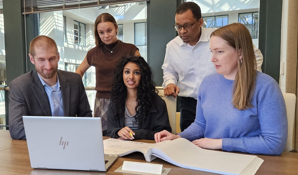 Five VHBers gather around a computer in a conference room to discuss a project.