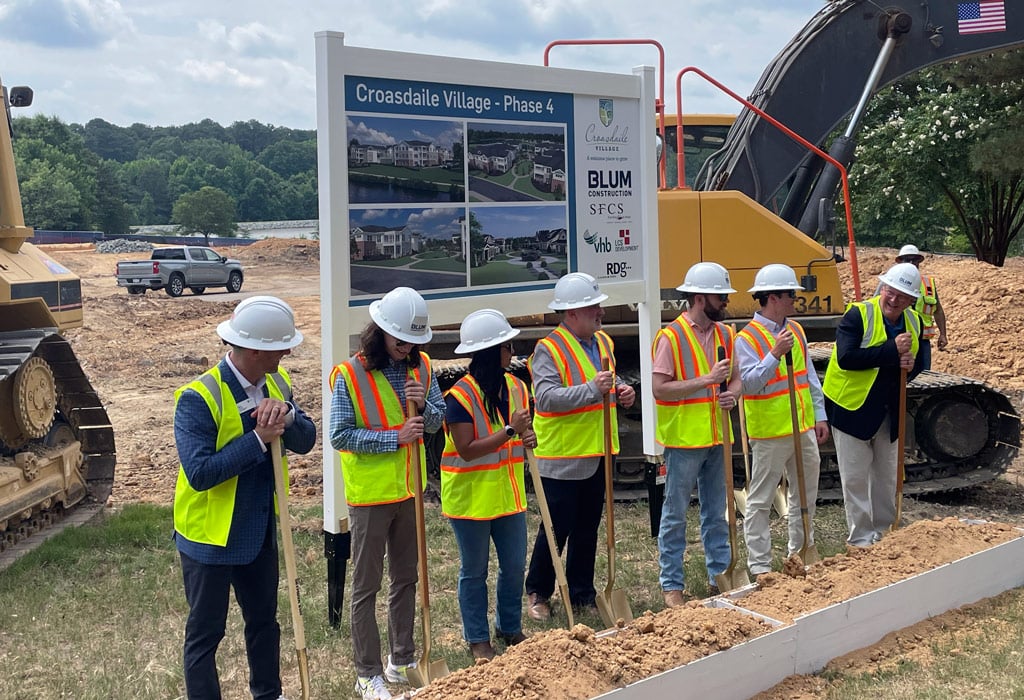 Groundbreaking ceremony with people in hard hats and safety vests holding shovels.