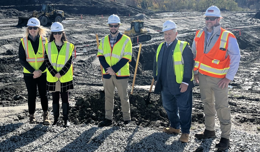 Five people in hardhats and safety vest holding shovels at a groundbreaking event.