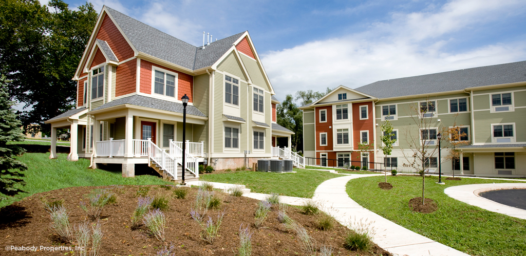 Green lawns in front of a red and grey apartment building. 