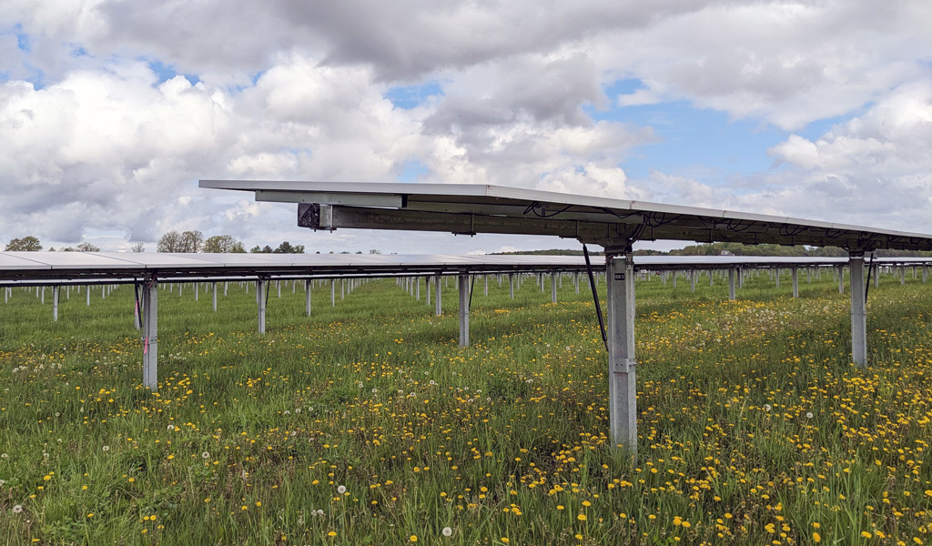 Solar panels installed in a green field under a cloudy sky.