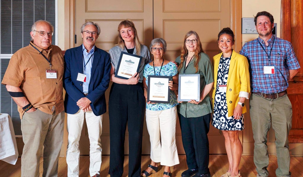 Group of people posing with awards at an event, standing in front of double doors.