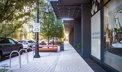 An urban sidewalk with a speed limit sign and bench.