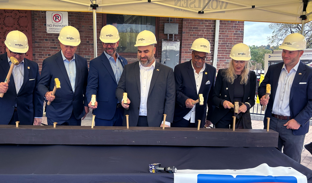 Seven individuals in hard hats using shovels for a ceremonial groundbreaking event, with banners from Wohlsen Construction and CT DOT visible.