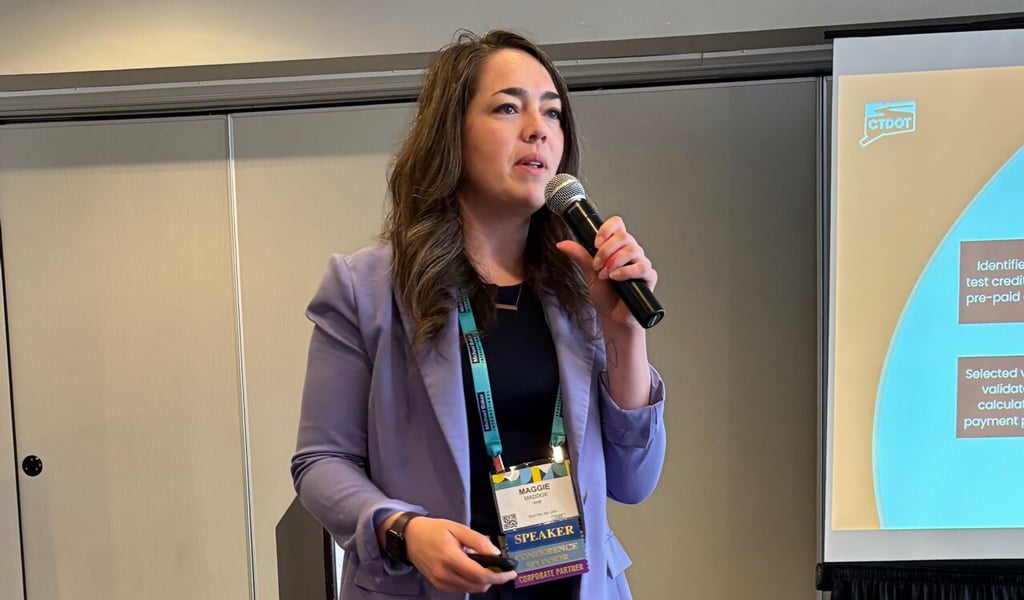 A person presenting at a conference, standing with a microphone in front of a projected presentation slide.