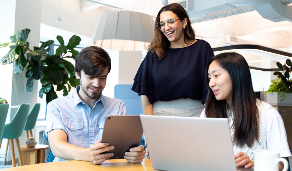 Three employees, standing and sitting, gathered around a computer.