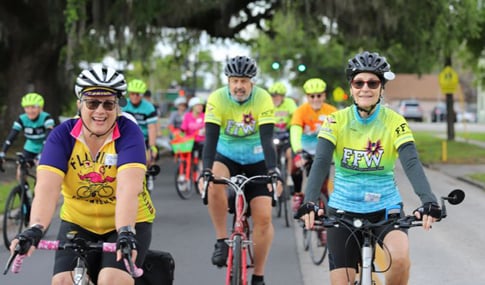 Colorfully dressed participants ride bicycles.