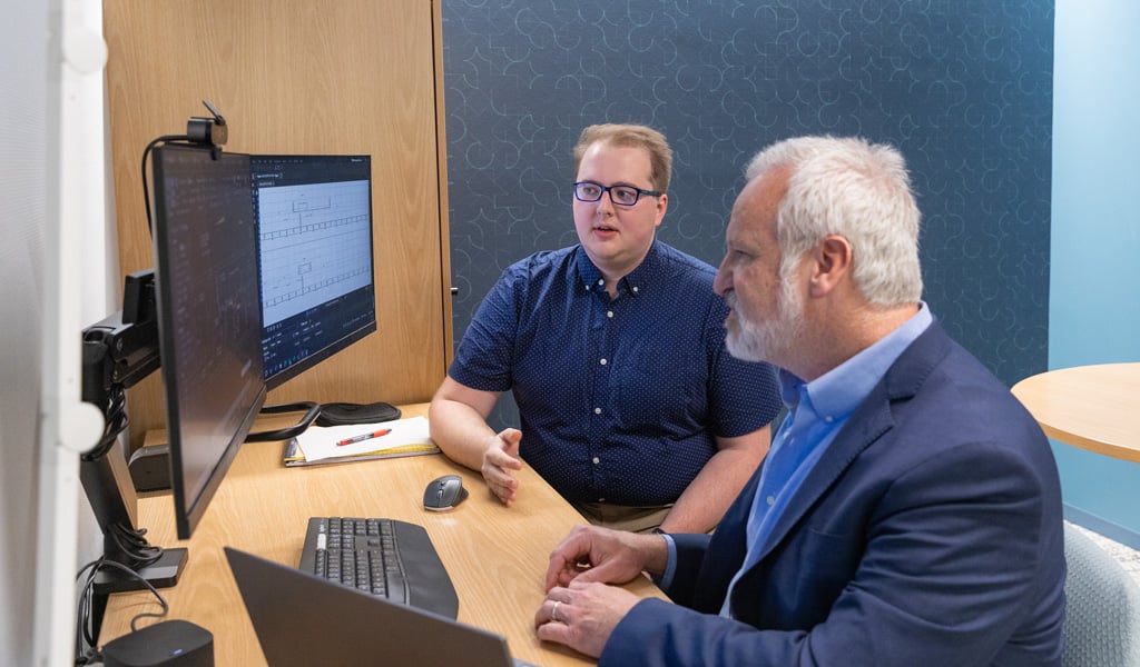 Gavin Graham meeting with his manager at a desk, reviewing project updates on computer screens