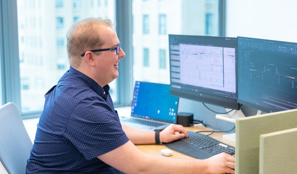 Gavin Graham working at his dual-monitor desk setup, focusing on transit design projects.