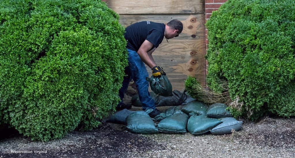 A man installs sandbags against boarded up windows and doors in preparation for a flood event. 