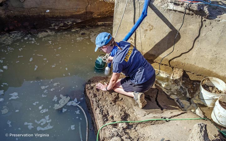 An archaeologist pumps water from one of the dig sites at Jamestown after a rain event