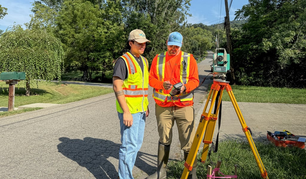 Two VHB team members in high-visibility vests reviewing survey equipment at a roadside structure in Western North Carolina.