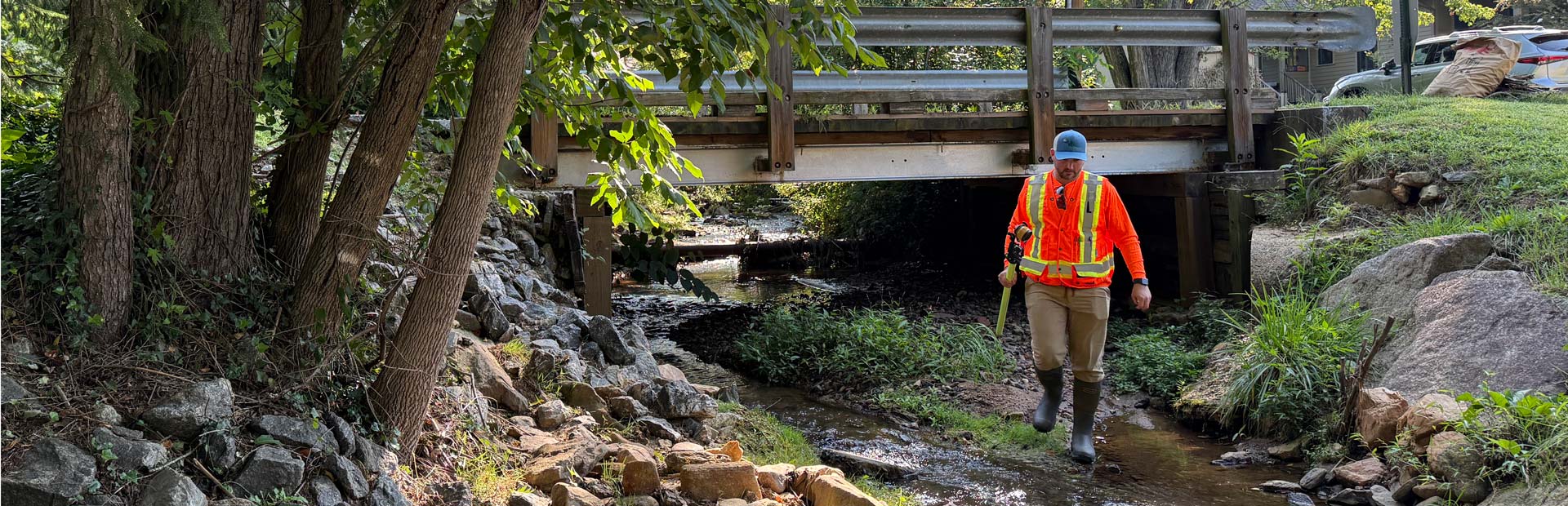 J.R. wading a shallow creek beneath a timber bridge during a hydraulic field investigation in Western North Carolina.
