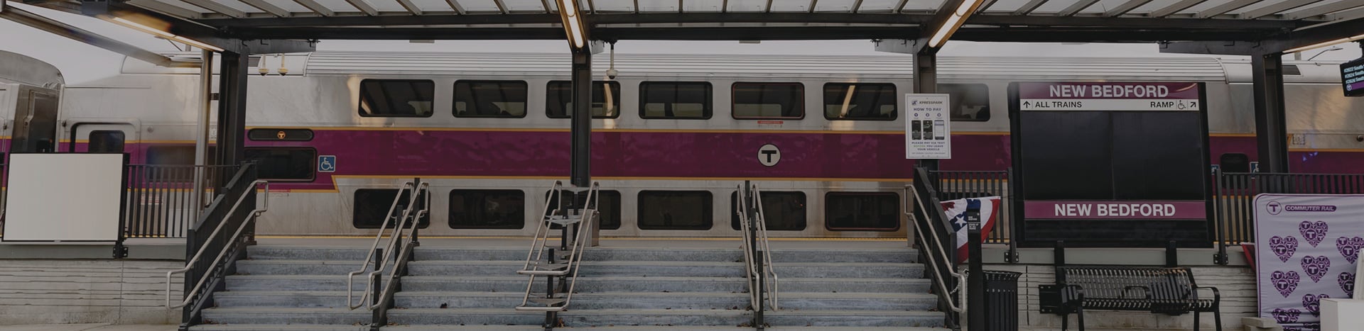 A train station covered by a modern canopy, with an MBTA commuter train in the background.