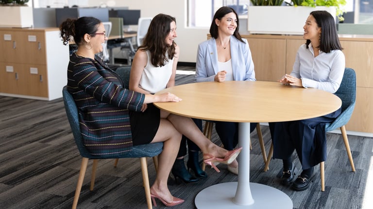Selma talks and laughs with three other women at a round table in an office.
