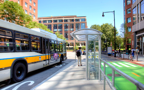 A bus drops off a passenger while bicyclists pedestrians use designated travel lanes and sidewalks.