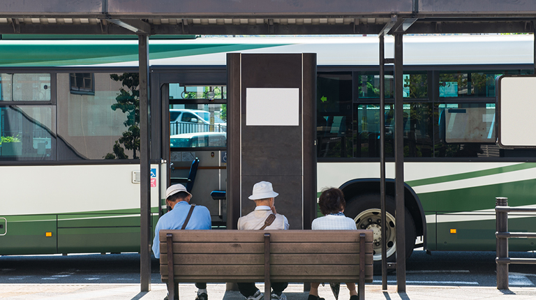Transit riders wait on a bench as a bus approaches the bus stop.