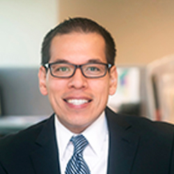 Carlos Vargas smiling in a suit and tie. 