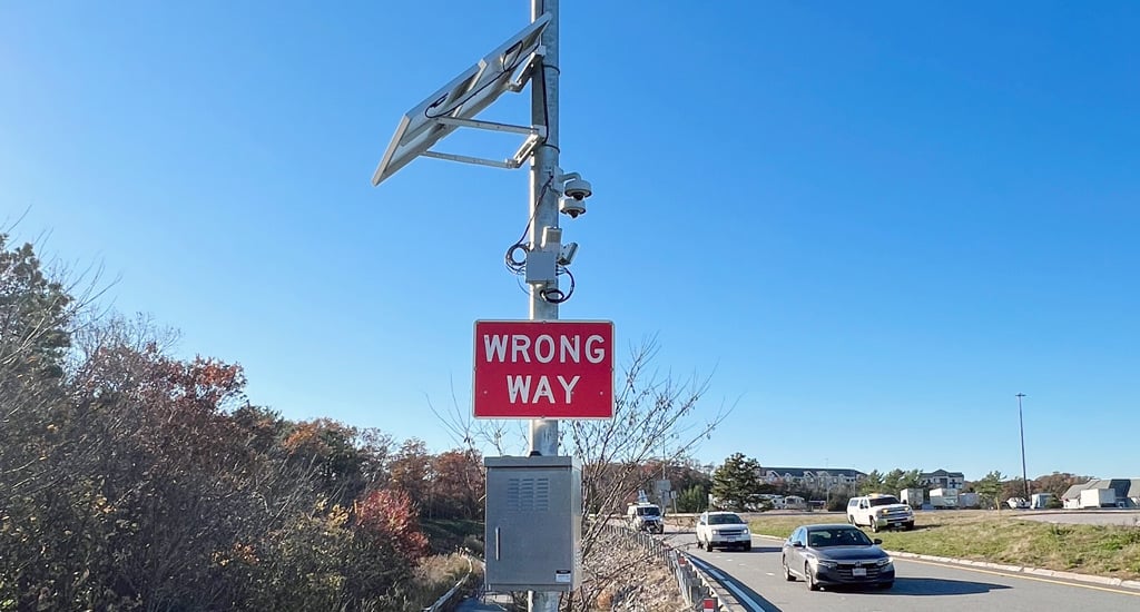 Wrong-way driving detection system with cameras, solar panels, and warning sign beside roadway.