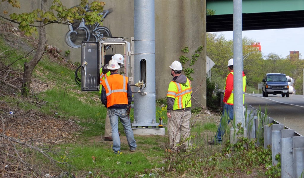 Field personnel inspect roadside communications equipment during ITS infrastructure installation.