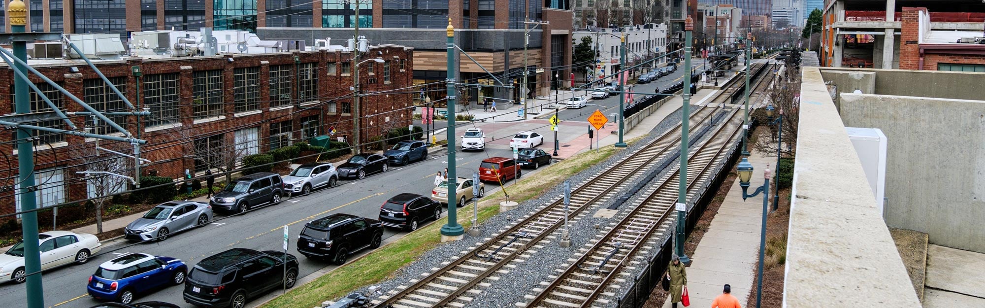 Urban redevelopment district with parallel light-rail tracks, busy roadway, modern office building, and construction site.