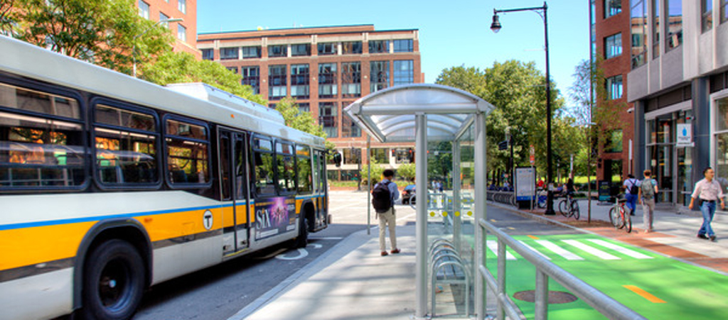 A downtown street featuring a bus stop, bike lane, and pedestrians on a sidewalk